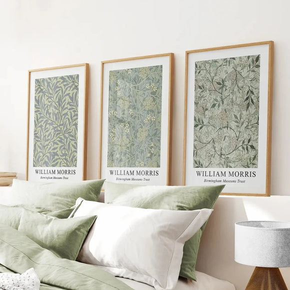 Three framed prints by William Morris on a wall above a bed with green and white bedding.