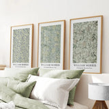 Three framed prints by William Morris on a wall above a bed with green and white bedding.