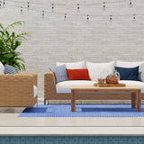 Outdoor patio with a white sofa, wicker chair, and wooden coffee table by a pool.