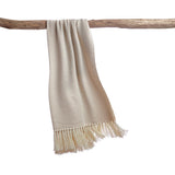 Beige woven blanket with fringes draped over a wooden branch on a white background