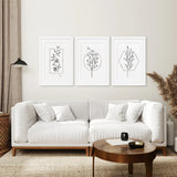 Living room with a white sofa, wooden coffee table, and framed Minimal Flower Line Art: Black White Wall Art Set on the wall.