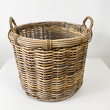 A natural woven wicker basket with two loop handles, shown on a clean white background.