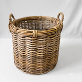 A natural woven wicker basket with two loop handles, shown on a light gray studio background.
