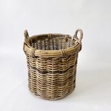 A natural woven wicker basket with two loop handles, shown on a plain white studio background.