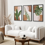Living room with a white sofa, round wooden coffee table, and three framed 3 Piece Terracotta Boho Wall Art. Green Tropical Leaves on the wall.