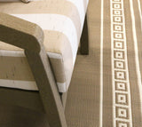 Close-up of a textured Border White Sand Outdoor Rug with geometric pattern next to a chair.