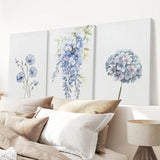 Floral wall art panels above a bed with pillows and a lamp.