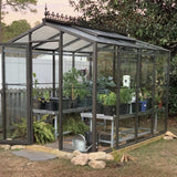 Janco Greenhouse with plants inside, surrounded by trees and garden elements.