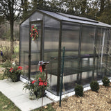 Janco Greenhouse with decorative wreath and flowers in a garden setting