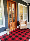 Front porch with wooden door, wicker chair, and red and black Buffalo Plaid Red & Black checkered rug.
