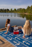Two women sitting on a dock by a lake with a Anchor Blue & White rug, cooler and drinks.