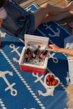 Person opening a cooler with Coca-Cola bottles on a blue anchor-patterned rug.