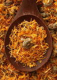 Wooden spoon filled with dried Orange Calendula (Calendula officinalis) flowers on a bed of marigold petals.