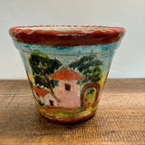 Casita Talavera Pot with artistic depiction of a house and trees on a wooden surface.