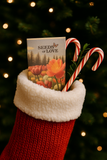 Red Christmas stocking with a packet of 'Seeds of Love' and candy canes against a blurred Christmas tree background.