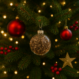 Decorative Christmas tree with red ornaments, a clear hanging ornament, and gold star against a blurred light background. Native Wildflower Seed Ornaments (3-Pack) – Holiday Gift Set | 100% Pollinator-Friendly, Non-GMO Heritage Mix