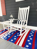 White rocking chair on a red, white, and blue striped rug with star pattern on a porch.