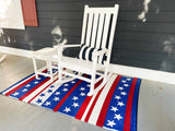 White rocking chair on a porch with a red, white, and blue striped rug featuring stars.