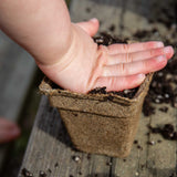 Hand holding a CowPots® #3 Square on a wooden surface