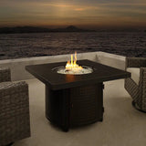 Clayton 40" Round Hammered Aluminum Convertible Gas Fire Pit Table with flames on a patio overlooking water at dusk