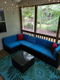Blue sectional sofa with red cushions on a patio with string lights and a TV in the background. Daisy Aqua & Green rug
