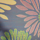 Close-up of a fabric with a floral pattern featuring pink, green, and yellow leaves on a blue background. Daisy Violet outdoor mat