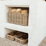Natural woven wicker baskets arranged inside a white outdoor fireplace or hearth, with wood logs visible in the top basket and additional baskets on the lower shelf over a gravel surface.