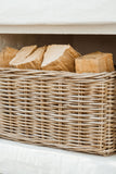 A natural woven wicker basket filled with cut firewood logs, set against a white textured background.