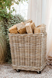 Wicker basket filled with firewood on a pebbled surface with greenery in the background