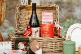 Wicker picnic basket with wine bottle, mug, and decorative items on a wooden table.