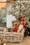 Wicker basket with decorative items including a plaid bow and pinecones on a wooden surface.