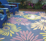 Floral-patterned mat on a deck with blue chairs and garden in the background