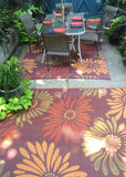 Outdoor dining area with a floral-patterned Daisy Rust rug, chairs, and a table.