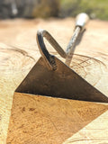 A close-up of a Dutch Weeder, Right or Left Handed with a looped handle resting on a cut wood stump outdoors.