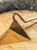 A close-up of a metal hand tool with a hooked end resting on a cut wood surface, showing a textured bronze-toned head and a silver metal handle against a blurred outdoor background.
