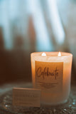 Candle with a 'Celebrate' label on a glass surface, blurred background