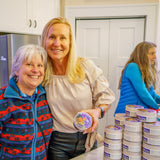Two women standing next to a stack of containers in a kitchen.
