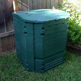 Green compost bin in a garden setting with grass and plants around.