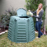 Person pouring contents into a large green compost bin outdoors.