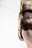 Close-up of a person's face partially obscured by a woven basket on a white background
