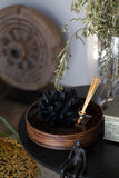 Decorative item with black pinecone, gold incense sticks, and green leaves on a dark surface.