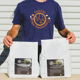 Person wearing a blue t-shirt with a logo, holding two white bags labeled 'Catalyst Bio Amendments'.