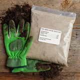 Green gardening gloves with soil next to a bag of Gaea Green Glacier Rock Dust on a wooden surface