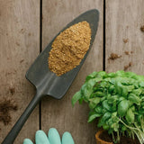 Gardening tool with Fish Meal on a wooden surface next to a potted plant