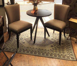 Round wooden table with two upholstered chairs on a Turkish Black & Brown patterned rug in a room.