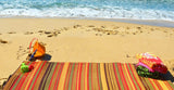 Beach scene with striped towel, colorful bag, and sand toys on a sandy beach with ocean waves. Stripes Warm Brown