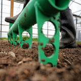 Person using a green Broadfork in soil, likely in a greenhouse setting