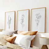 Boho Botanical Art Prints | Set of 3 Green Leaves on a wall above a bed with pillows and a lamp.