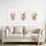 Beige sofa with decorative pillows and a blanket, featuring three framed Neutral Watercolor Wildflower Art Prints Set on a white wall.