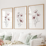 Three floral prints in wooden frames on a wall above a sofa.